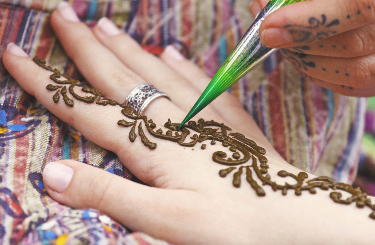 Artist painting traditional indian henna tattoo on woman hand, closeup picture, focus on mehndi artwork