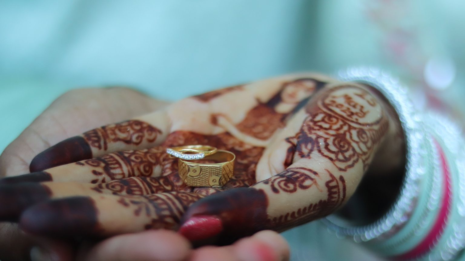 A closeup of a bride's hand painted with henna with golden wedding rings in it