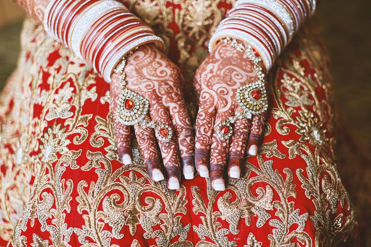 The close-up shot of Indian bride with beautiful pink saree showing mehndi (henna) hand with a lot of glitter bracelets (bangles) on her wrist